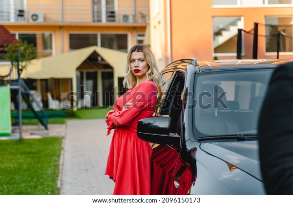 Side view portrait of one woman\
Caucasian adult looking to the camera angry while leaning on the\
car with hands crossed wearing dress outdoor in summer\
day