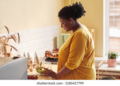 Side View Portrait Of Overweight Black Woman Cooking Healthy Meal In Kitchen Lit By Sunlight, Copy Space