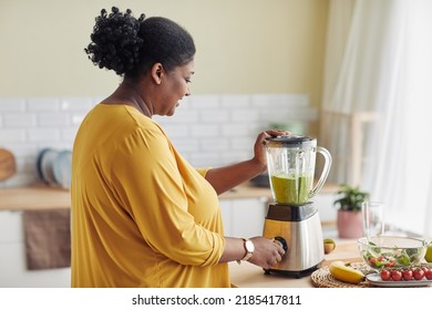 Side view portrait of overweight black woman using blender while making healthy smoothie at home kitchen, copy space - Powered by Shutterstock