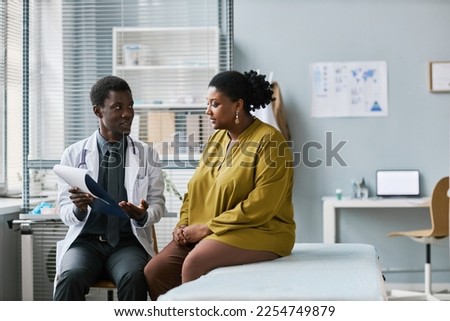 Side view portrait of overweight black woman talking to doctor in medical clinic, copy space