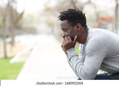 Side view portrait of a pensive serious black man looking away sitting on a park bench - Powered by Shutterstock