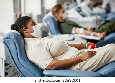 Side view portrait of people wearing masks while giving blood in row at medical donation center