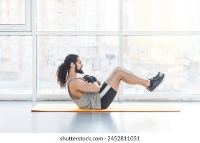 Side view portrait of powerful man with curly long hair having workout in gym doing crunches, wearing sportswear, sit-ups for training abdominal muscles. Indoor shot with window on background. - Powered by Shutterstock