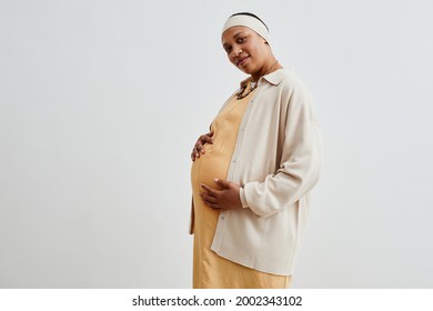 Side view portrait of pregnant African-American woman looking at camera while standing against white background, copy space