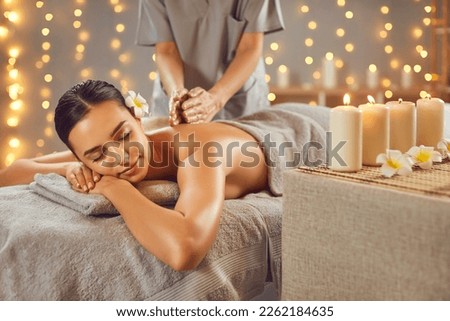 Side view portrait of a pretty young brunette woman with closed eyes relaxing in spa salon getting massage. Therapist doing back treatment procedure. Wellness and beauty day concept.