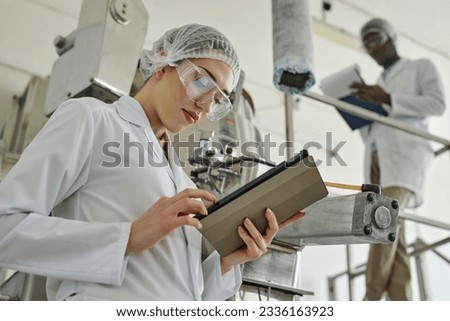 Side view portrait of pretty young woman wearing lab coat and using digital tablet in modern factory workshop, copy space