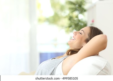 Side view portrait of a relaxed person laughing sitting on a couch in the living room at home with a window and a green background - Shutterstock ID 499585105