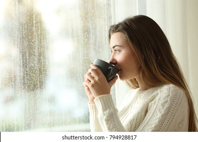 Side View Portrait Of A Relaxed Teen Drinking Coffee Looking Outside Through A Window In A Rainy Day Of Winter At Home