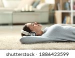 Side view portrait of a relaxed woman listening to music with headphones lying on a carpet at home