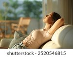 Side view portrait of a relaxed woman sitting in a sofa at sunset at home