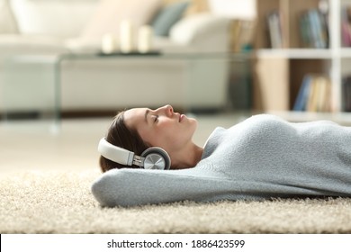 Side view portrait of a relaxed woman listening to music with headphones lying on a carpet at home