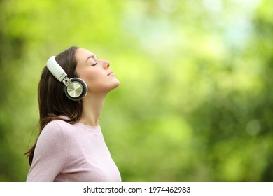Side view portrait of a relaxed woman meditating listening audio guide with wireless headphones in a park or forest