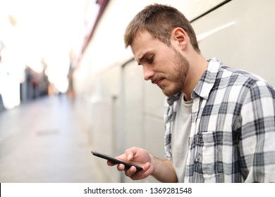 Side View Portrait Of A Sad Man In A Lonely Street Using A Smart Phone