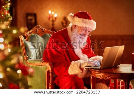 Side view portrait of Santa Claus using laptop by Christmas tree and smiling, copy space