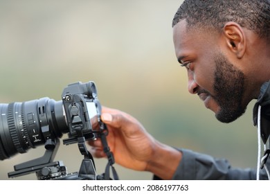 Side view portrait of a satisfied man with black skin checking photos on mirrorless camera