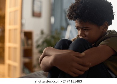 Side view portrait of scared young child crying and hugging knees hiding in room copy space