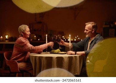 Side view portrait of senior couple enjoying romantic dinner at home and clinking wine glasses at candlelit table copy space - Powered by Shutterstock