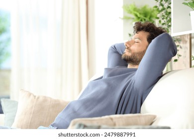 Side view portrait of a serious man resting and relaxing sitting on a sofa at home