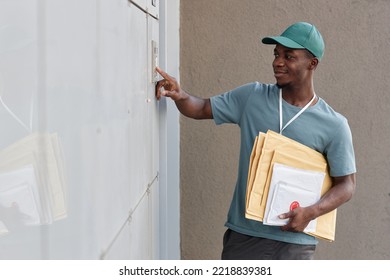 Side View Portrait Of Smiling Delivery Worker Ringing Doorbell And Holding Packages