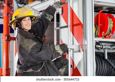 Side View Portrait Of Smiling Female Firefighter Standing On Truck At Fire Station