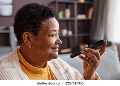 Side view portrait of smiling senior woman recording voice message via smartphone at home, copy space - Powered by Shutterstock