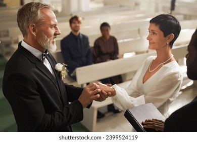 Side view portrait of smiling senior couple exchanging rings during wedding ceremony in church - Powered by Shutterstock