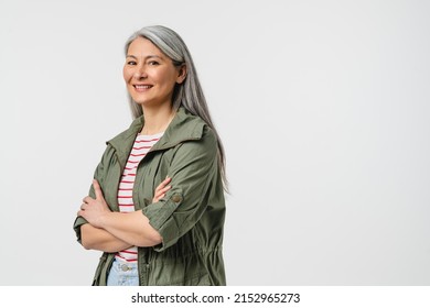 Side view portrait of a smiling with toothy smile mature middle-aged woman in casual clothes with grey hair looking at camera crossing arms isolated in white background - Powered by Shutterstock