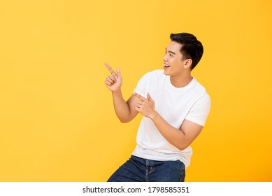 Side View Portrait Of Smiling Young Handsome Asian Man Pointing Fingers In Empty Space Aside In Isolated Studio Yellow Background