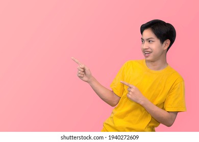 Side View Portrait Of Smiling Young Handsome Asian Man Pointing Fingers In Empty Space Aside In Isolated Studio Pink Background