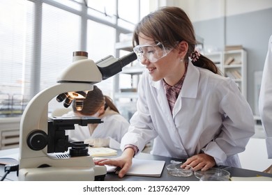 Side view portrait of smiling young girl looking into microscope while enjoying experiments in school chemistry lab - Powered by Shutterstock