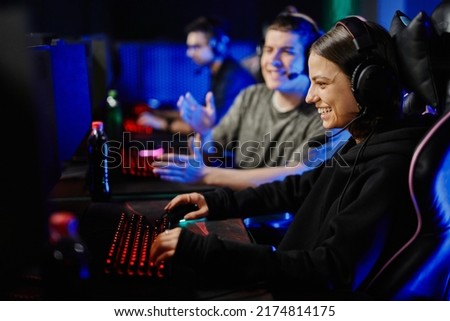 Side view portrait of smiling young woman playing video games on PC with cyber sport team cheering