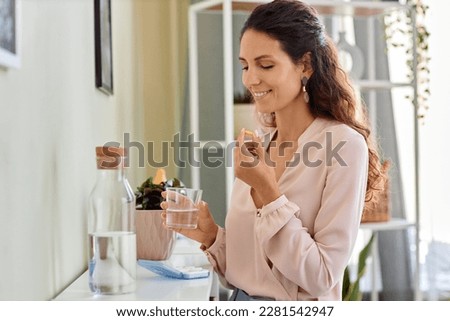 Side view portrait of smiling young woman taking vitamins and drinking water in morning