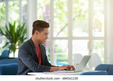 Side View Portrait Of Successful Asian Man Using Modern Laptop At Home For Work And Smiling