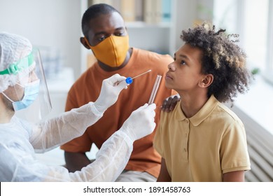 Side View Portrait Of Teenage African-American Boy Taking Covid Test In Clinic With Male Nurse Holding Swab And Glass Tube