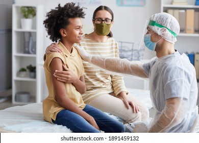 Side View Portrait Of Teenage African-American Boy Smiling After Covid Vaccination In Clinic With Male Nurse Congratulating Him