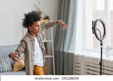 Side View Portrait Of Teenage African-American Boy Filming Videos At Home And Dancing To Camera Set On Ring Light, Young Blogger Concept, Copy Space