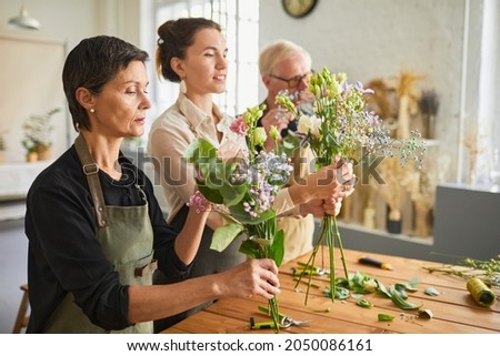 Side view portrait of three florists arraigning flower compositions in cozy workshop, copy space