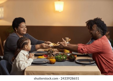 Side view portrait of three generation African American family enjoying dinner together in cozy home and sharing food over table  - Powered by Shutterstock