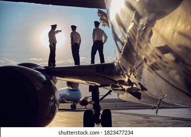 Side view portrait of three unrecognizable persons looking to the sunny sky while standing on the wing of big passenger airplane
