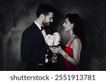 Side view portrait of trendy rich gentleman in tux with bow roses to joyful, lady in purple dress with earring, lovely romantic couple isolated on grey background. Wedding marriage engagement concept