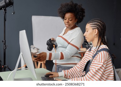 Side view portrait of two African American young women as female photographers collaborating in photo studio and looking at pictures on computer screen - Powered by Shutterstock