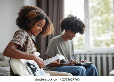 Side view portrait of two African-American teenagers playing electric guitars at home and smiling happily, brother and sister concept, copy space - Powered by Shutterstock