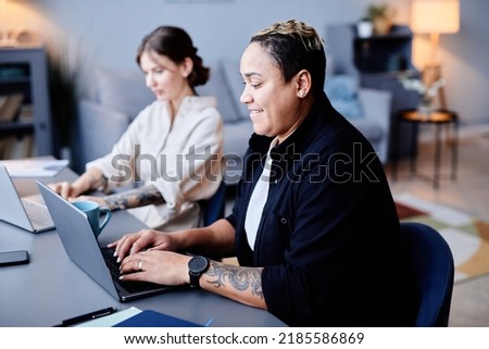 Side view portrait of two modern women using computers at home workplace together and smiling