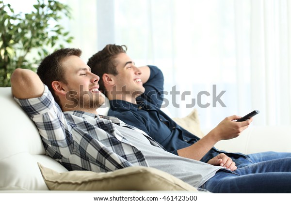 Side view portrait of two\
roommates watching tv sitting in a comfortable sofa in the living\
room at home