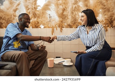 Side view portrait of two smiling business people shaking hands greeting each other during business meeting in office lounge