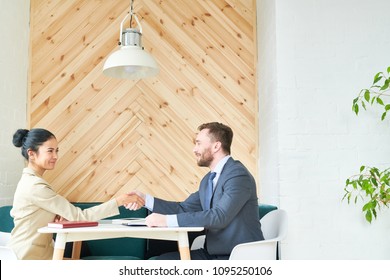 Side View Portrait Of Two Successful Business People, Man And Woman, Shaking Hands Across Table During Meeting In Cafe, Copy Space