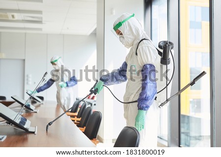 Side view portrait of two workers wearing hazmat suits disinfecting conference room in office, copy space
