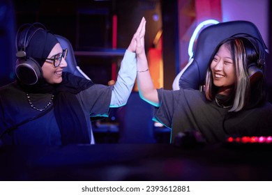 Side view portrait of two young women playing video games together and high five celebrating victory in cybersports club