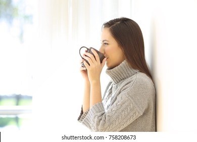 Side view portrait of a woman drinking coffee looking through a window in a house interior - Powered by Shutterstock