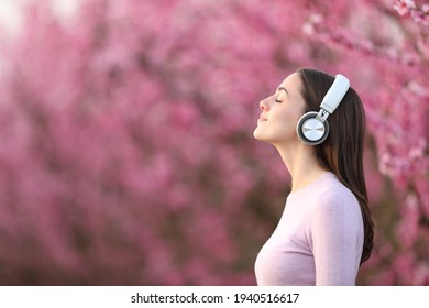 Side view portrait of a woman relaxing listening to music with wireless headphones in a pink field
